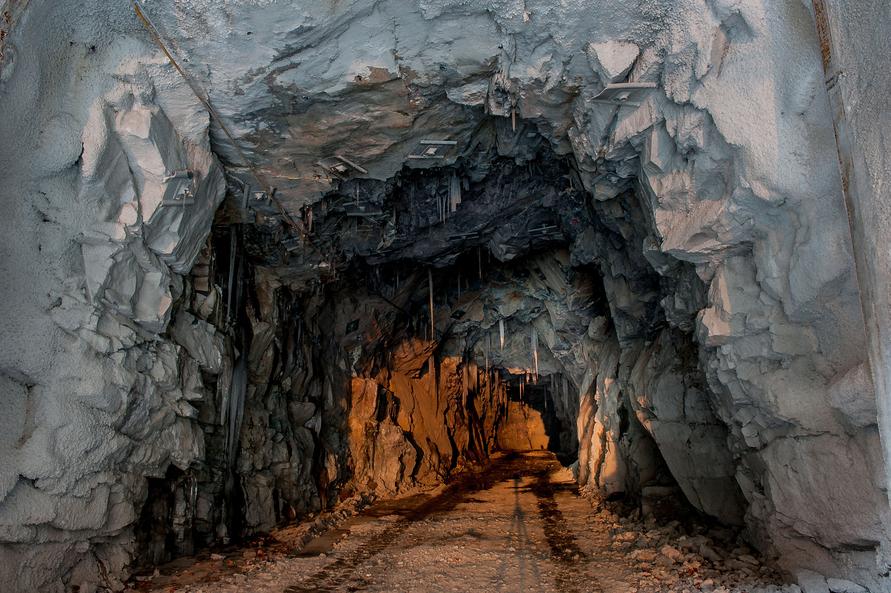Dark mineral tunnel with irregular rock walls and an illuminated tunnel floor leading toward the tunnel entrance.
