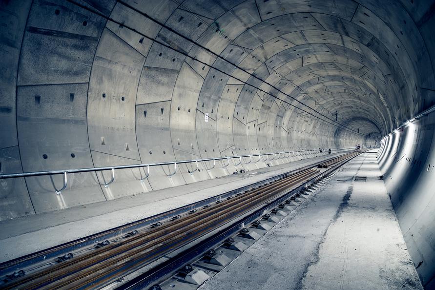 View of a long, empty tunnel with concrete walls and railway tracks down the center, illuminated by soft lighting.