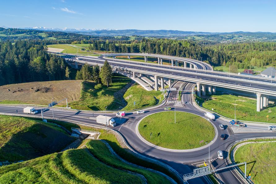 Aerial view of a highway interchange with multiple roadways and a roundabout surrounded by forests and grassland.