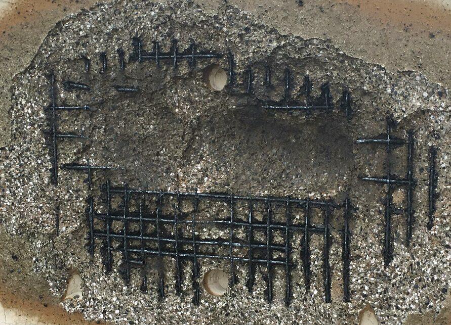 Close-up of a textured surface with embedded black nails arranged in a grid pattern against a gray backdrop.