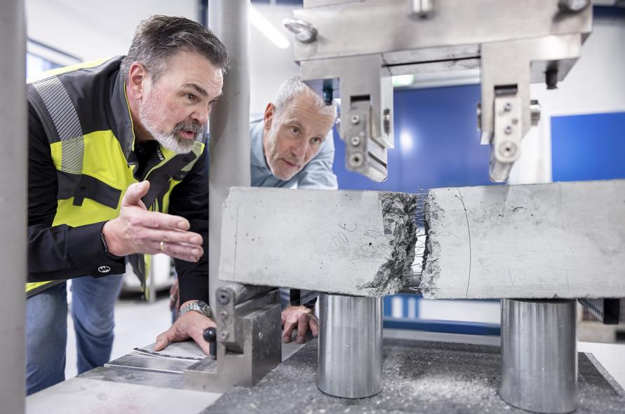 Two men observe a metal specimen being tested for pressure in a laboratory setting, examining the results closely.